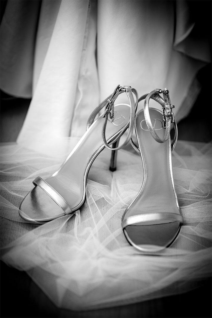Detailaufnahme silberner High-Heel-Sandaletten auf einem Tüllstoff.