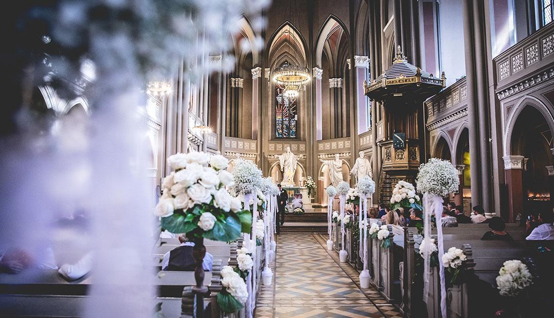 Blick durch den mit weißen Blumen geschmückten Mittelgang einer Kirche zum Altar.