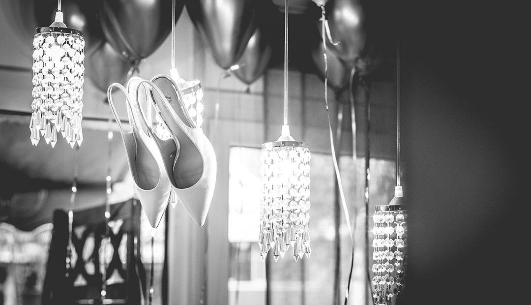 Hängende Kristalllüster, dazwischen hohe weiße Brautschuhe und schwarze Luftballons.