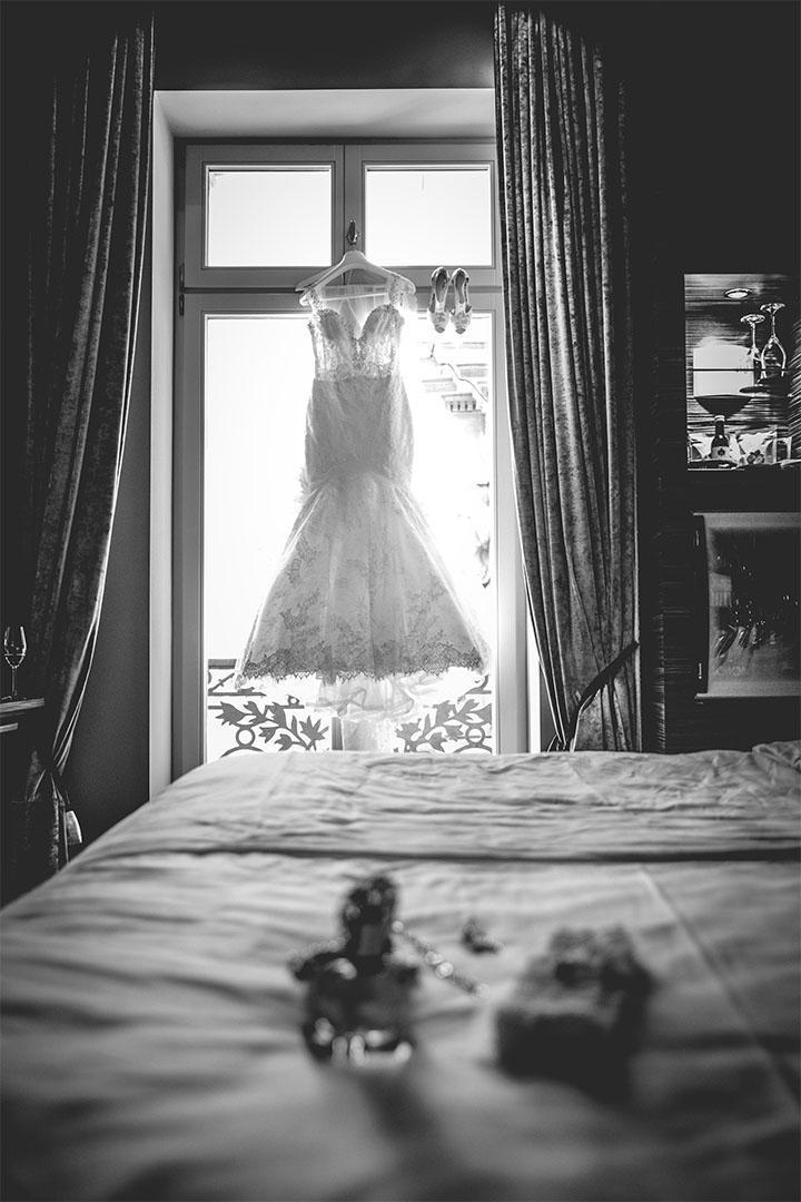 Brautkleid und Schuhe hängen hinterleuchtet vor einem Fenster, schwarz-weiß fotografiert.